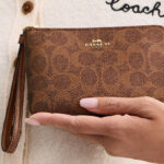 A Woman Holding Coach Outlet Corner Zip Wristlet In Signature Canvas in Brown Copper