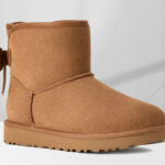 UGG Womens Ultra Mini Bailey Leather Bow Boot in Chestnut Color on the Table