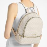 A Woman Wearing Michael Kors Rhea Medium Signature Logo Backpack in Cream Multi