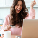 A Woman Joyfully Holding a Credit Card While Using a Laptop