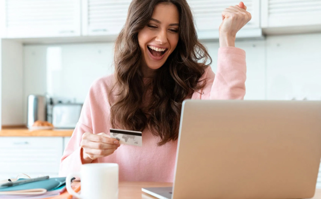 A Woman Joyfully Holding a Credit Card While Using a Laptop