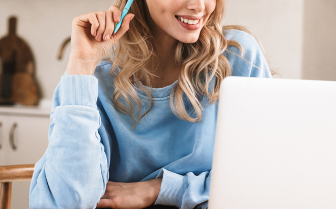 A Smiling Woman Holding a Pen and Looking at Her Laptop