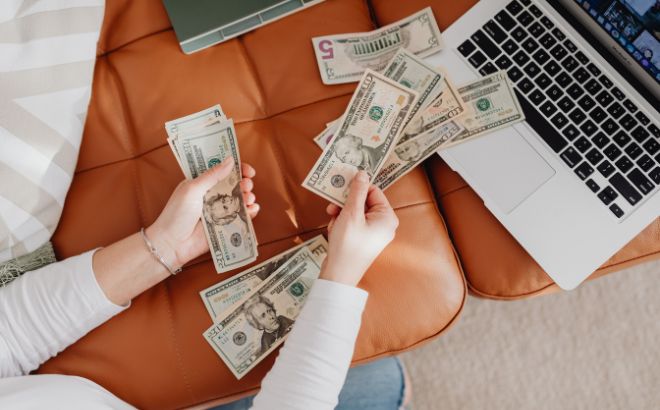 A Person Counting Cash and Budgeting on a Laptop A Person Counting Cash and Budgeting on a Laptop